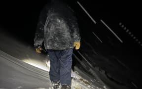A man walks through snow and darkness on the Tongariro Alpine Crossing.