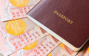 one hundred new zealand cash money bank note on table with red cover passport book