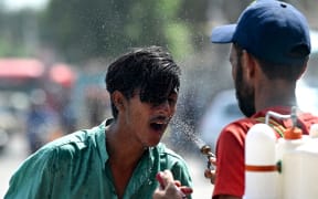 A volunteer sprays water on a bypasser's face along a street during a hot summer day in Karachi on May 30, 2024, amid the ongoing heatwave. (Photo by Asif HASSAN / AFP)