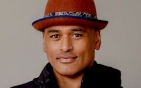 Image of Murdoch Ngahau smiling softly at camera. He wears a small brown rimmed hat and black jacket.