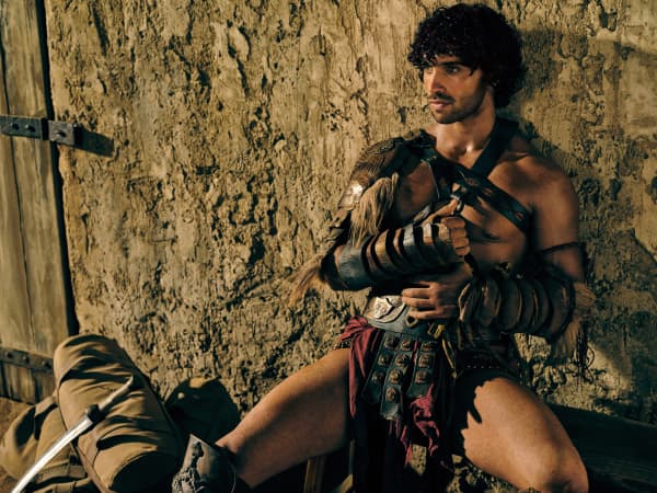 Jordi Webber, wearing a gladiator costume, leans against a wall with his legs open.