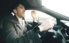A man in a grey jacket sings in the car while driving.