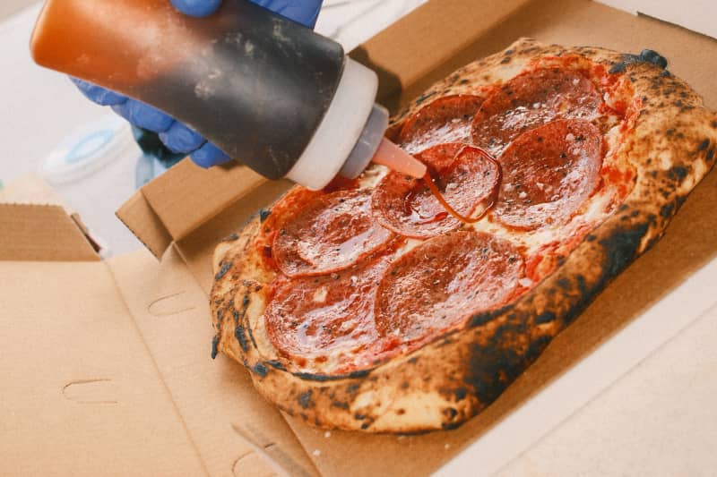 A person pouring sauce from a bottle on Bari's Pizza halal pepperoni pizza.