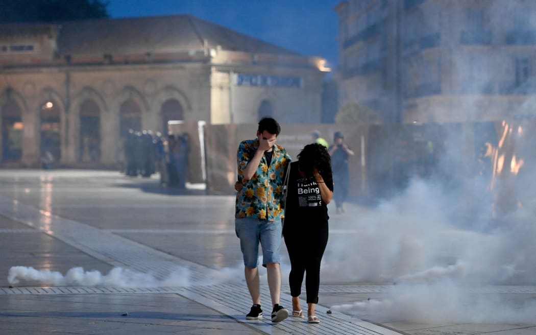 A man and a woman cover their noses from teargas fumes during a protest in Montpellier, southern France on June 30, 2023, over the shooting of a teenage driver by French police in a Paris suburb on June 27. French President Emmanuel Macron has announced measures including more police and urged parents to keep minors off the streets as he battled to contain nightly riots over a teenager's fatal shooting by an officer in a traffic stop. (Photo by Sylvain THOMAS / AFP)