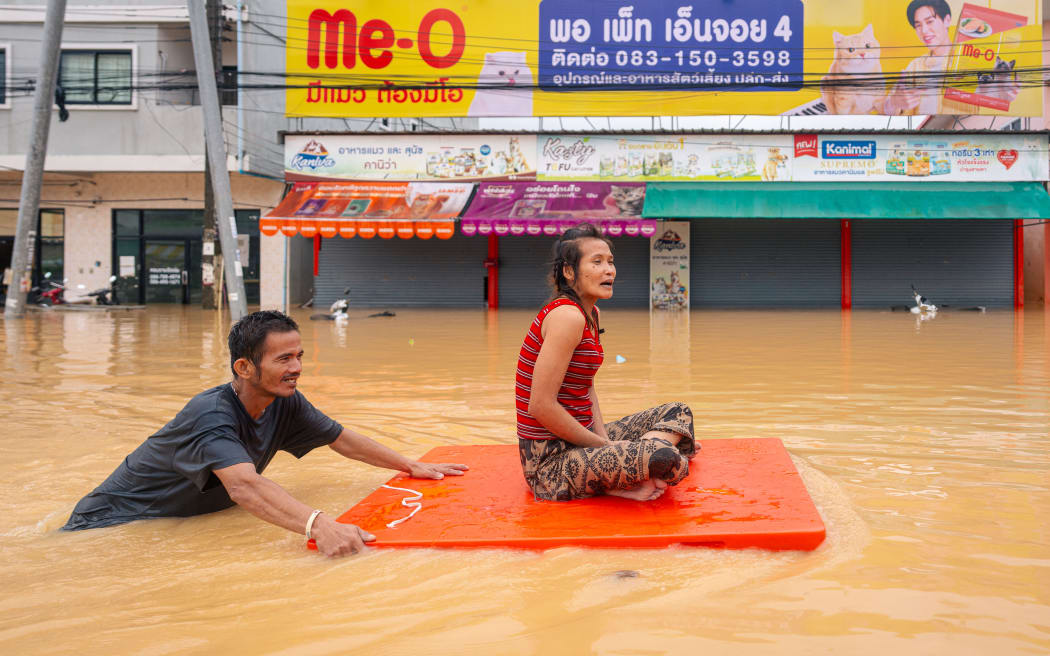A man transports a woman through flood waters in Hat Yai in Thailand's southern Songkhla province on November 26, 2025, as severe flooding affected thousands of people in the country's south following days of heavy rain. Tens of thousands of people in Thailand and neighbouring Malaysia were displaced by widespread flooding, with streets submerged, homes inundated and at least 34 dead, officials said November 26. (Photo by Arnun Chonmahatrakool / THAI NEWS PIX / AFP)