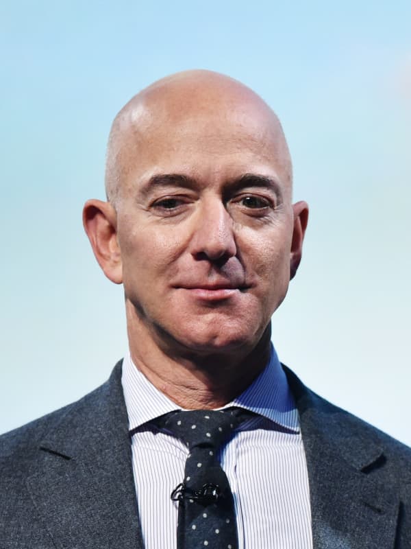 Jeff Bezos - a bald man in a suit - looks downward and wears a slight smile.
