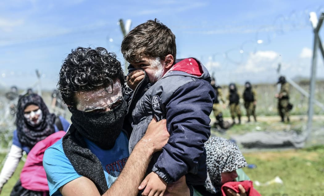 A family with toothpaste smeared over their faces as a protection against teargas, moves to safety as refugees and migrants clash with Macedonian police.
