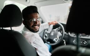 rear view, young man driving his car, looking at camera