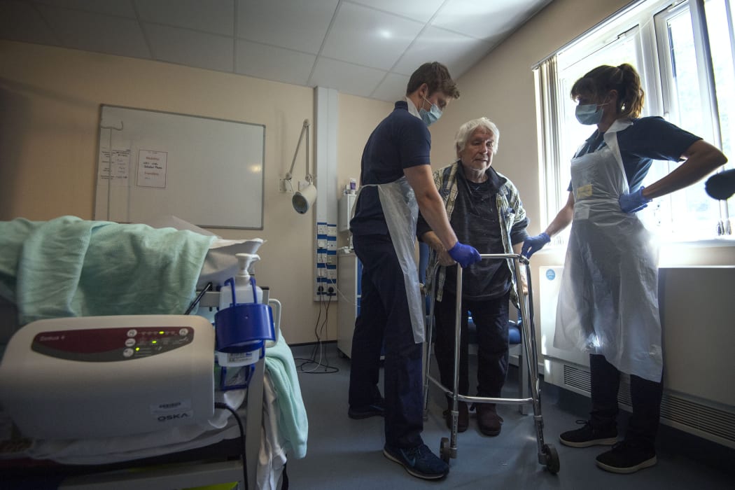 Rehab support workers perform physiotherapy on Michael Kidd, 82, at a new UK facility for Covid-19 patients who no longer need acute care.