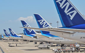 This photo taken on July 23, 2023 shows a worker (bottom L) on the tarmac behind a line of planes for Japanese airline All Nippon Airways (ANA) at Tokyo International Airport at Haneda in Tokyo. ANA Holdings are expected to announce first quarter earnings on July 28. (Photo by Richard A. Brooks / AFP)