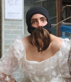 An image of performer Jess Holly-Bates, wearing a wedding dress, a black balaclava and giant false moustache.