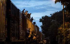 Undocumented migrants climb on a train known as "La Bestia".
