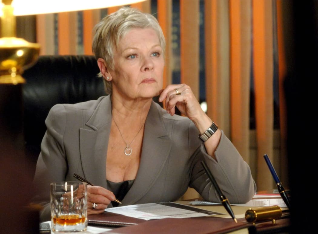 Dame Judi Dench wears a grey suit and an inscrutable look.