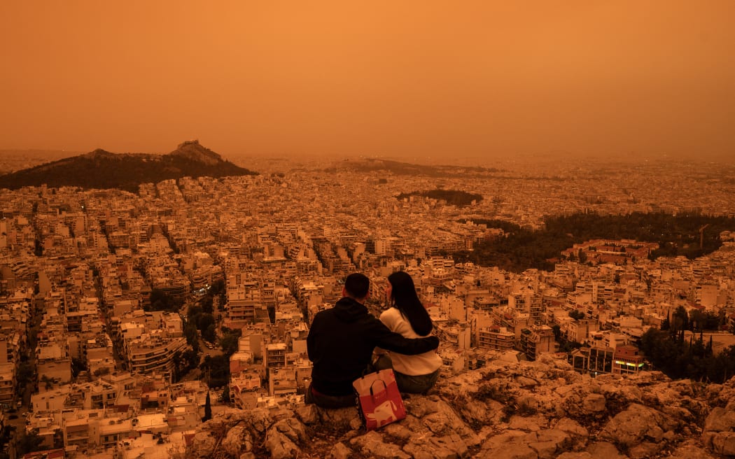 A couple sits on Tourkovounia hill, as southerly winds carry waves of Saharan dust, in Athens, on April 23, 2024. Clouds of dust blown in from the Sahara covered Athens and other Greek cities on April 23, 2024, one of the worst such episodes to hit the country since 2018, officials said. The yellow-orange haze smothered several regions, limiting visibility and prompting warnings of breathing risks from the authorities. (Photo by Angelos TZORTZINIS / AFP)
