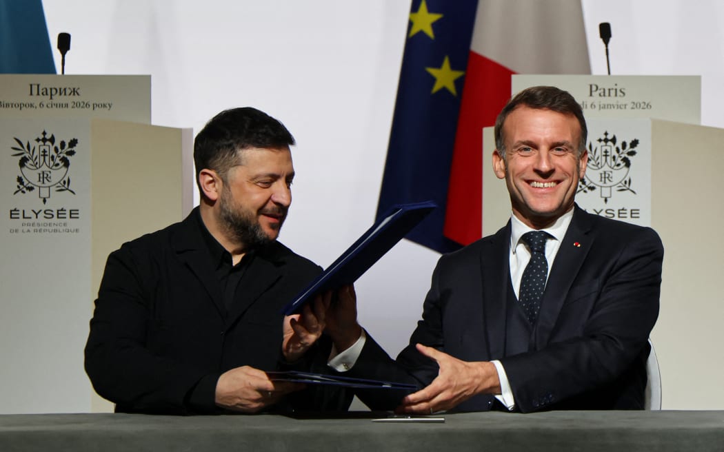 Ukraine's President Volodymyr Zelensky (L) and France's President Emmanuel Macron react alongside Britain's Prime Minister upon the signing of the declaration on deploying post-ceasefire force in Ukraine during the Coalition of the Willing summit on security guarantees for Ukraine, at the Elysee Palace in Paris, on January 6, 2026. The summit of the group of Ukraine supporters dubbed the "Coalition of the Willing" is the latest of several meetings planned for the new year as diplomatic efforts to end Europe's deadliest conflict since World War II have gained pace in recent weeks.