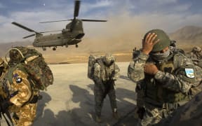 US Army soldiers from 2-506 Infantry 101st Airborne Division, Afghan National Army soldiers and a New Zealand Army soldier take cover as a CH-47 Chinook helicopter lands to transport them to the Spira mountains in Khost province, in November 2008.