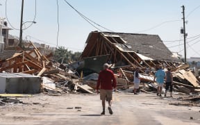 People walk along a street blocked by a building after Hurricane Michael passed through the area.