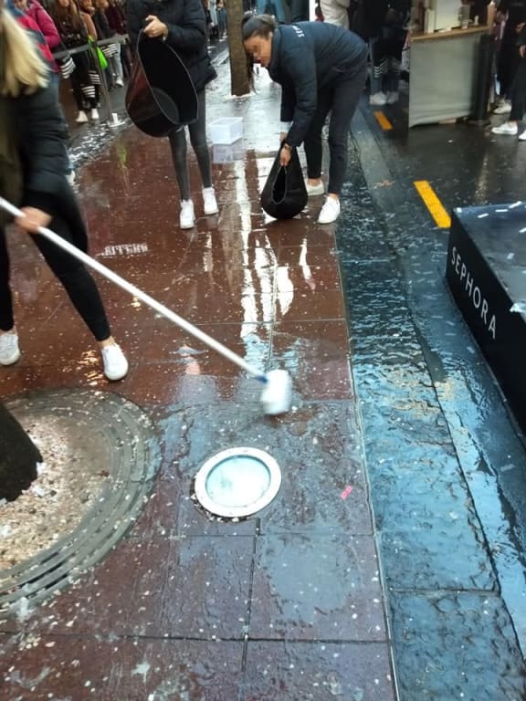 Sephora staff sweep debris into the drains in Auckland.