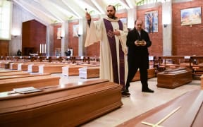 Priest Don Marcello gives a blessing to the coffins of deceased people inside the church of San Giuseppe in Seriate, on March 28, 2020.
