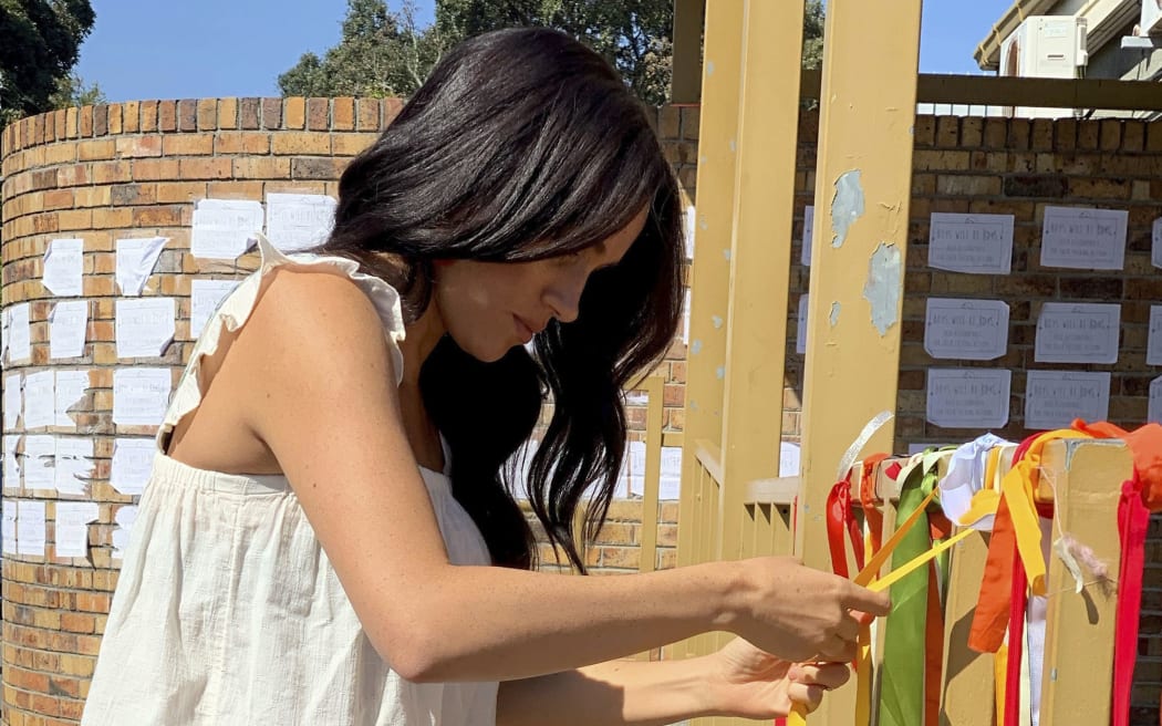A recent undated handout photograph released on September 28, 2019 by the Duke and Duchess of Sussex shows Britain's Meghan, Duchess of Sussex ties on a ribbon as she visits the memorial to murdered South African student Uyinene Mrwetyana in Cape Town. -