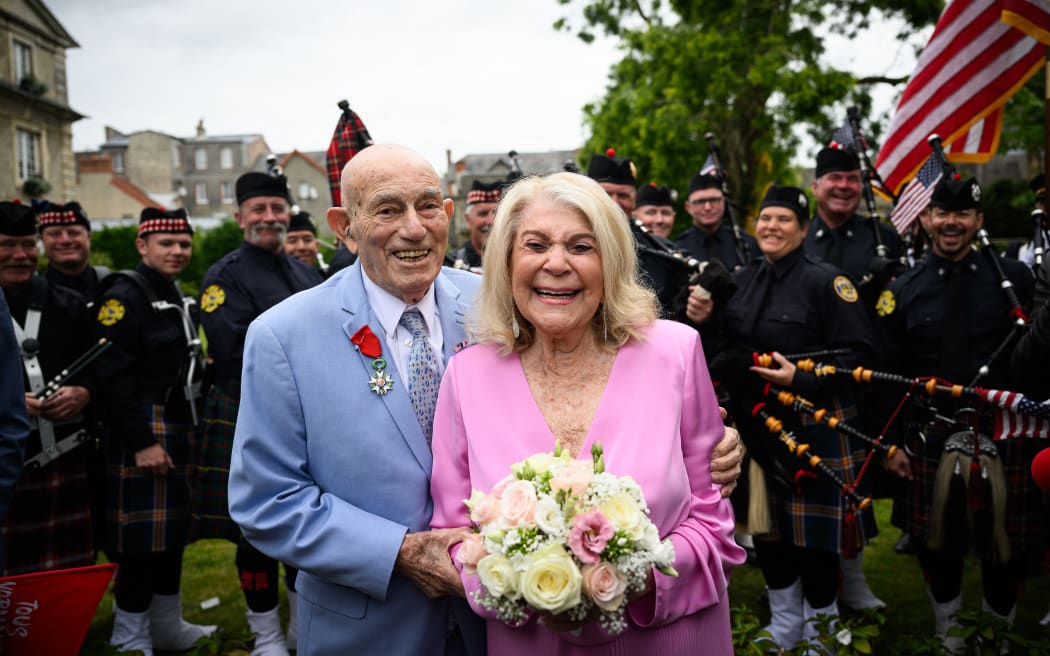 Newly-weds Jeanne Swerlin, 96, (R) and US WWII veteran Harold Terens, 100, (L) pose for photographs in front of a piper band as they celebrate their marriage during a wedding at the town hall of Carentan-les-Marais, in Normandy, northwestern France, on 8 June, 2024, just days after being honoured on the 80th anniversary of the D-Day landings that took place a few kilometres away. The D-Day ceremonies on 6 June 2024 marked the 80th anniversary since the launch of 'Operation Overlord', a vast military operation by Allied forces in Normandy, which turned the tide of World War II, eventually leading to the liberation of occupied France and the end of the war against Nazi Germany.