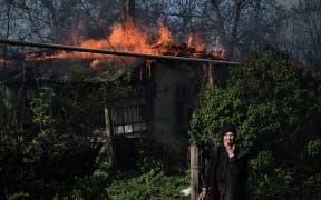 An elderly woman stands outside a burning house after shelling in the town of Chasiv Yar, Donetsk region, on May 7, 2023, amid the Russian invasion of Ukraine. (Photo by Sergey SHESTAK / AFP)