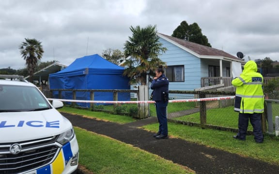 Police are executing a search warrant at a house on Taraire Street in relation to the investigation into the homicide of Linda Woods. At least four officers are guarding the cordoned house and other officers can be seen rummaging through rubbish bins on the property.