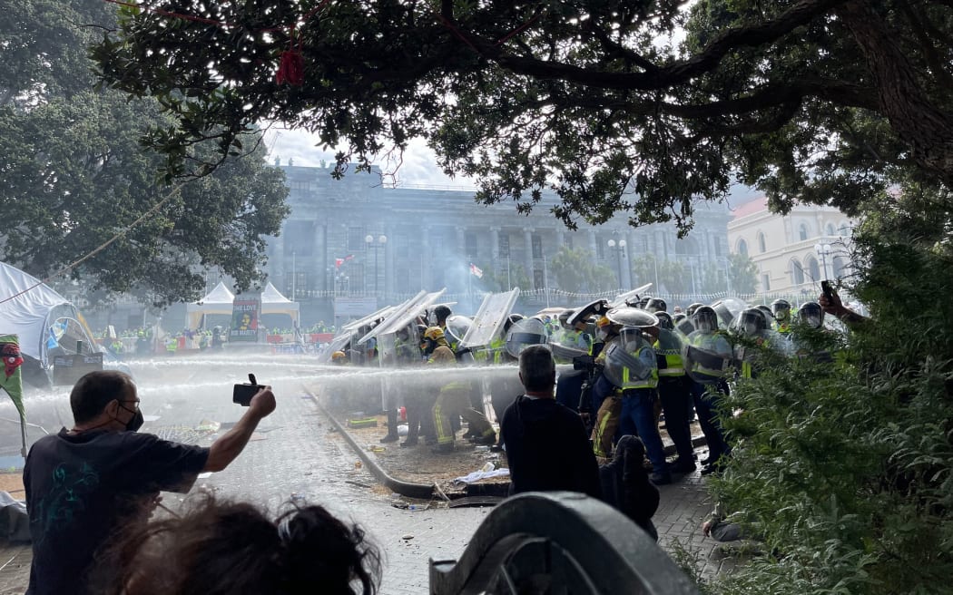 Police using hoses on the fire from behind riot shields.