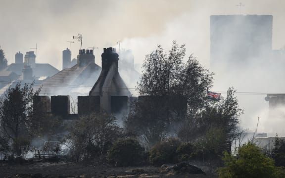 A Union Flag flies amongst the smouldering ruins of houses as fire services tackle a large blaze on 19 July 2022 in Wennington, England. A series of grass fires broke out around the British capital amid an intense heatwave.