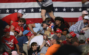 BUTLER, PENNSYLVANIA - JULY 13: Attendees duck from gunfire at a campaign rally for Republican presidential candidate, former U.S. President Donald Trump at Butler Farm Show Inc. on July 13, 2024 in Butler, Pennsylvania. Trump slumped before being whisked away by Secret Service with injuries visible to the side of his head. Butler County district attorney Richard Goldinger said the shooter and one audience member are dead and another was injured.
