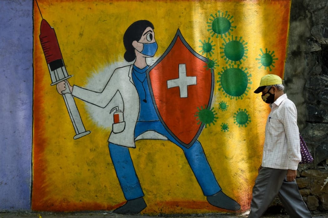 A resident walks past a wall mural depicting a health worker wearing a facemask while holding a vaccine and a shield to spread awareness about the Covid-19 coronavirus, in Mumbai on June 30, 2021.