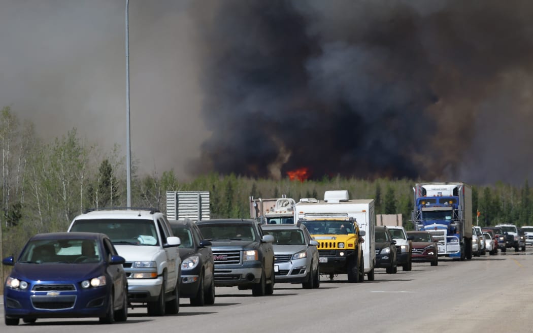 Evacuees drive south as flames and smoke rise along the highway near Fort McMurray, Alberta on Friday.