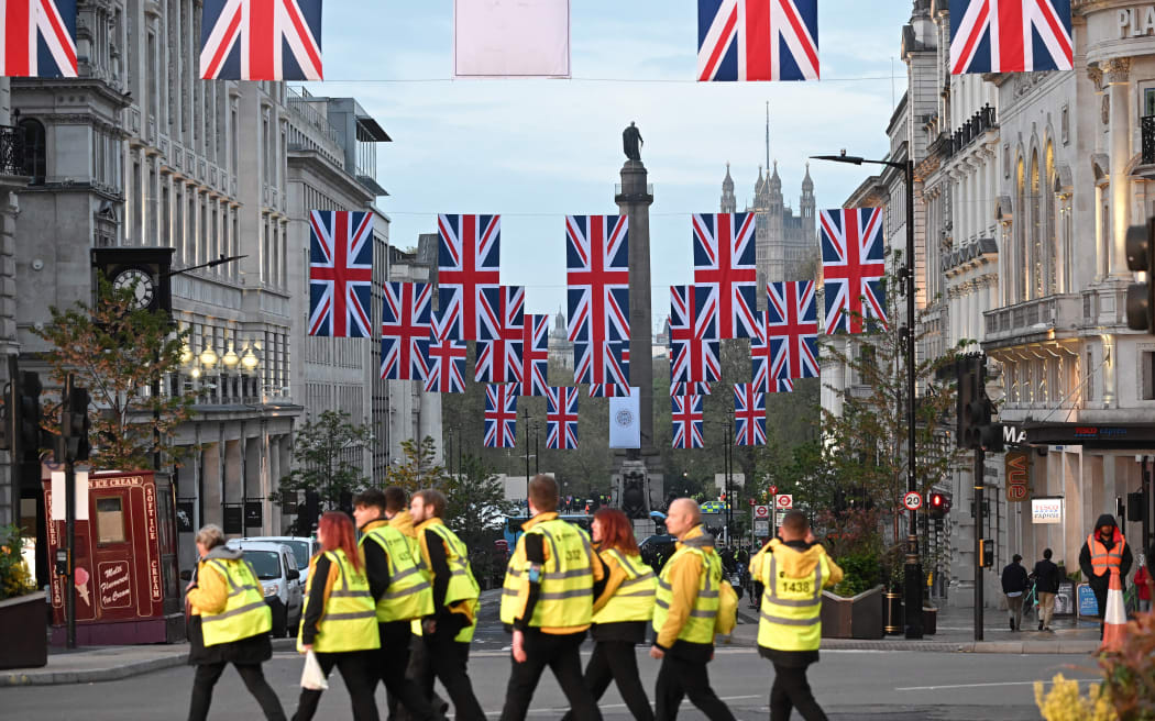 Workers cross the route of the 'King's Procession', a two kilometres stretch from Buckingham Palace to Westminster Abbey, as they wait for Britain's King Charles III and Britain's Camilla, Queen Consort to pass in the Diamond State Coach, in central London, on May 6, 2023 ahead of their coronations. - The set-piece coronation is the first in Britain in 70 years, and only the second in history to be televised. Charles will be the 40th reigning monarch to be crowned at the central London church since King William I in 1066. Outside the UK, he is also king of 14 other Commonwealth countries, including Australia, Canada and New Zealand. Camilla, his second wife, will be crowned queen alongside him and be known as Queen Camilla after the ceremony. (Photo by LOIC VENANCE / AFP)