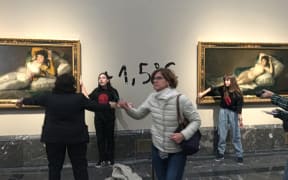 Two activists shown with hands glued to the frames of paintings by Francisco Goya at the Prado museum in Madrid, in a picture released by Extinction Rebellion on 5 November, 2022.