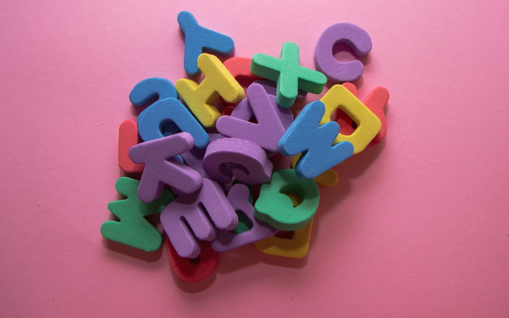 Colorful plastic alphabet letters on pink background, top view.