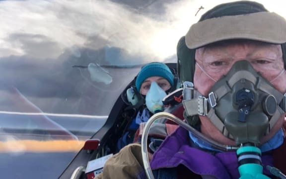 Two people, both wearing oxygen masks, in the cockpit of a glider.