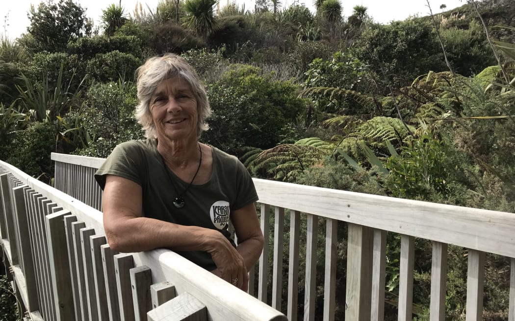 Linda stands on a bridge walkway with bush in the background. She wears a green Karioi project t-shirt.