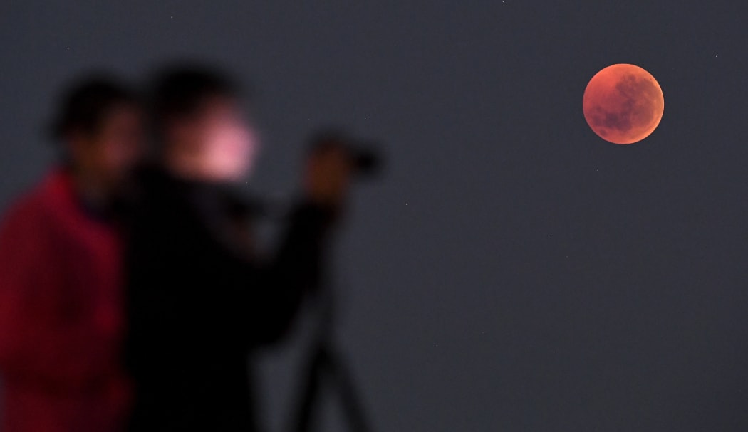 People gather to watch a "blood moon" eclipse in Melbourne on July 28, 2018. / AFP PHOTO / WILLIAM WEST