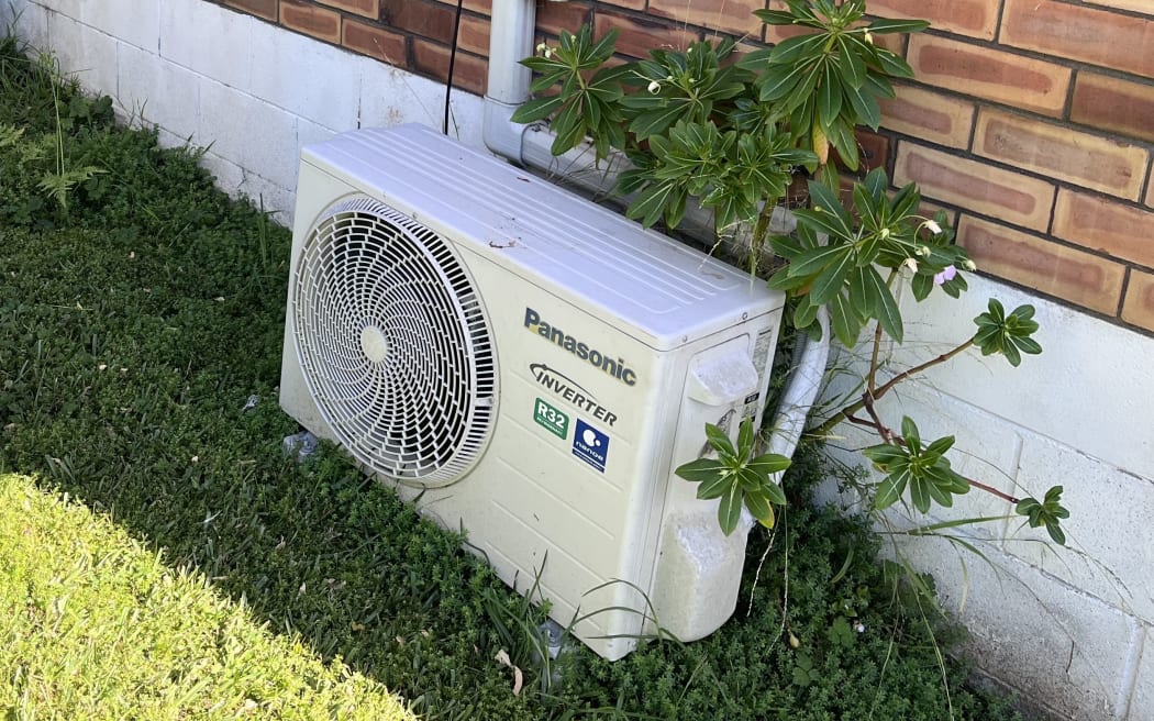 An external heat pump unit sits on the ground outside a house