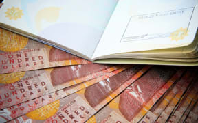one hundred new zealand cash money bank note on table with red cover passport book