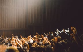 An audience in an auditorium, voting with raised hands.