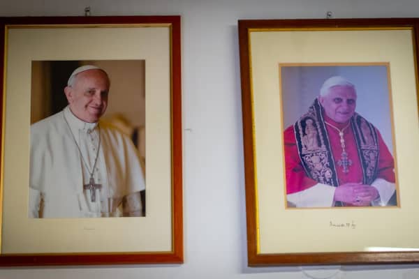 Framed pictures of Pope Francis and his predecessor Pope Benedict XVI hanging on a wall.