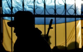 A Ukrainian soldier seen against his country's flag.