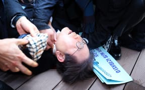 South Korean opposition party leader Lee Jae-myung is attended to after being attacked in Busan on January 2, 2024. South Korean opposition party leader Lee Jae-myung was attacked on January 2, while talking to reporters in the port city of Busan, Yonhap news agency reported. (Photo by YONHAP / AFP) / - South Korea OUT / NO ARCHIVES -  RESTRICTED TO SUBSCRIPTION USE  
 
IMAGES PIXELATED AT SOURCE