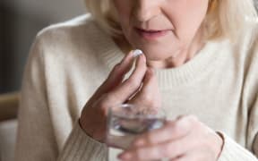 Close up of unhealthy middle aged woman suffers from pain, holding pill and glass of still water feels ill taking medicine, cropped image.