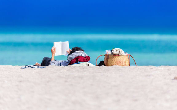 A person lies on the beach reading a book in the sun.