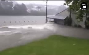 A CCTV screenshot of a field and clubrooms swamped with fast-moving flood waters.