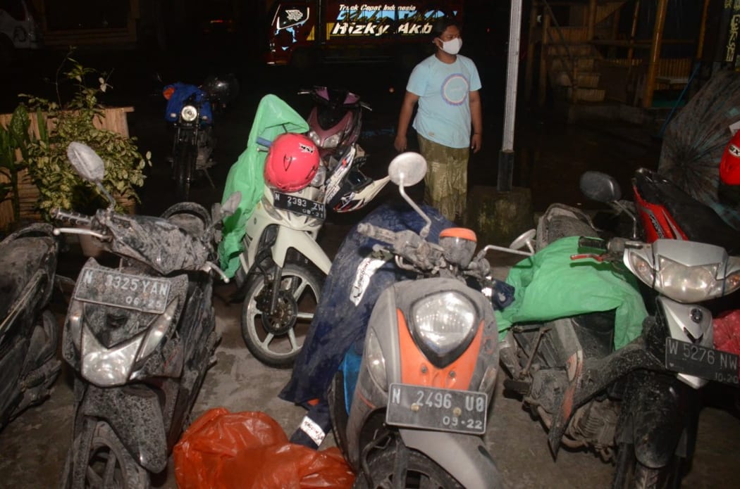 A villager walks past the motorbikes of evacuees covered by volcanic ashes at Sumberurip village, in Lumajang, on December 4, 2021, after the Semeru volcano eruption.