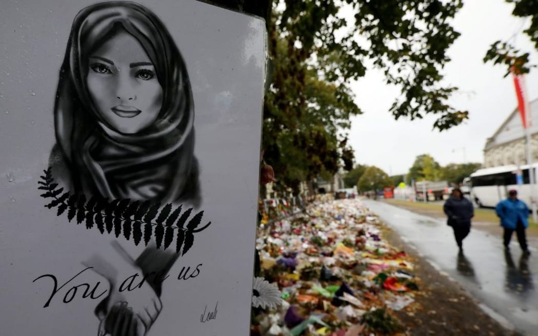 People walk past flowers and tributes displayed in memory of the twin mosque massacre victims outside the Botanical Gardens in Christchurch on April 5, 2019.