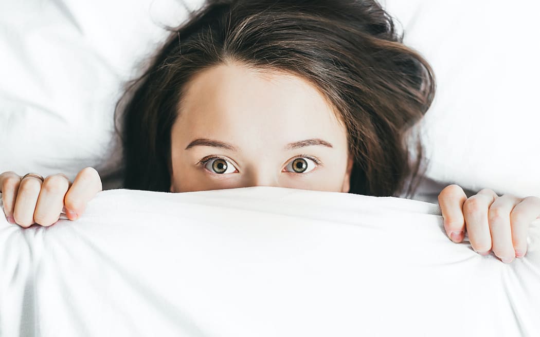 girl with dark hair hiding in bed